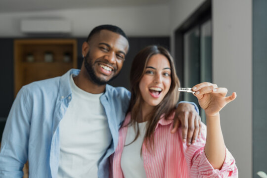 Happy young couple celebrates receiving keys to their new apartment, smiling and embracing in a modern interior. Image conveys joy, achievement, homeownership and the excitement of moving into a first