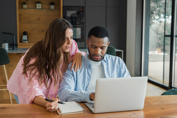 Obraz premium A young couple collaborates over a laptop and notebook in their kitchen, focused on budgeting, planning and decision making. The scene conveys teamwork, support, concentration and modern remote work l