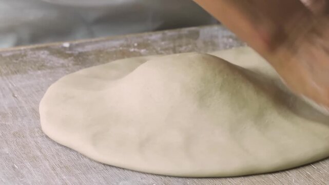 Close-up slow motion shot of a professional baker's hands skillfully kneading and stretching a fresh, pillowy ball of pizza dough on a floured wooden surface. The footage captures the traditional Neap