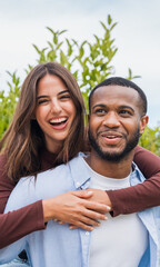 Happy young couple share a joyful embrace outdoors, laughing together in a casual romantic portrait that conveys love, connection, friendship and carefree moments in a natural garden setting.