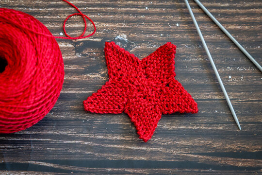 Knitted red star, knitting needles, and ball of red yarn on wooden table, top view, flat lay