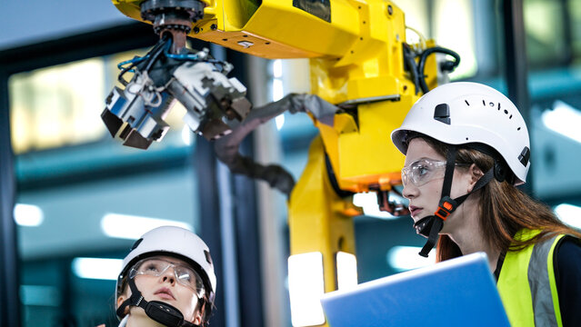 Two female robotics engineers in an R and D lab program an artificial intelligence system. They are testing the hardware and motion control of a large industrial robot.