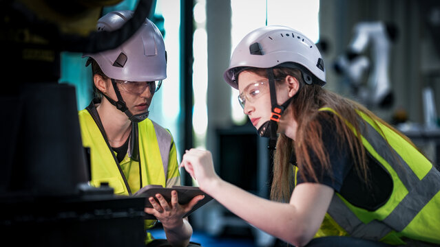 Two female robotics engineers in an R and D lab troubleshoot an artificial intelligence cobot. They are inspecting the robotic system hardware and programming.
