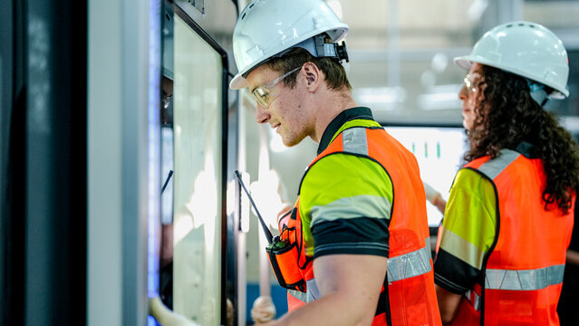 Two AI engineers, a man and woman, program an industrial robot. The woman points at the HMI screen, diagnosing a system alert in the smart factory cleanroom.