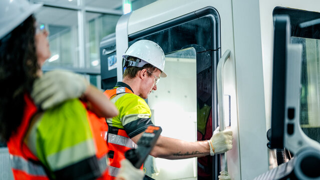 Two engineers program an industrial robot or CNC machine using an AI interface. The team manufactures advanced microchips or high tech components in a smart factory.