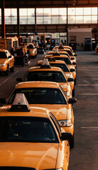 Fototapeta premium Yellow taxis line up inside large industrial building during sunset. Cars wait for service or new assignment in automotive assembly plant. Warm light streams through windows.