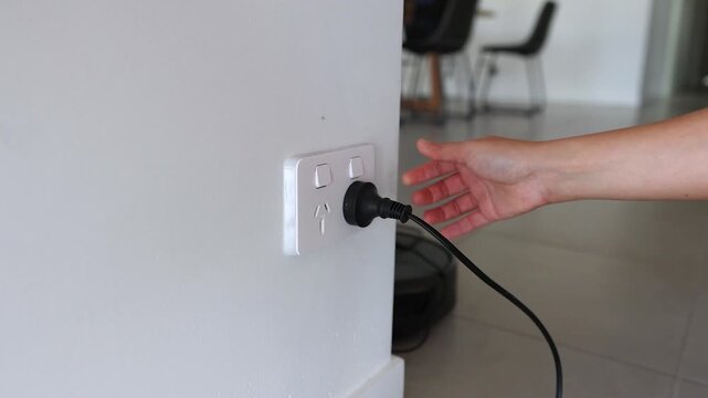 Close up of a hand unplugging a power cord from a wall socket with switches.