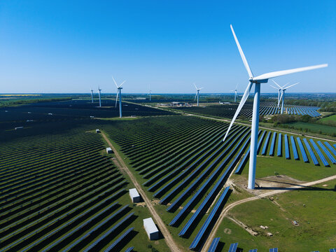 Aerial view of Chelveston Wind Farm featuring rows of solar panels and tall wind turbines under a clear blue sky in Wellingborough, England, United Kingdom.