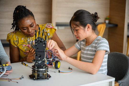 Mentor instructing student assembling robotic hand and wiring electronics in STEM class