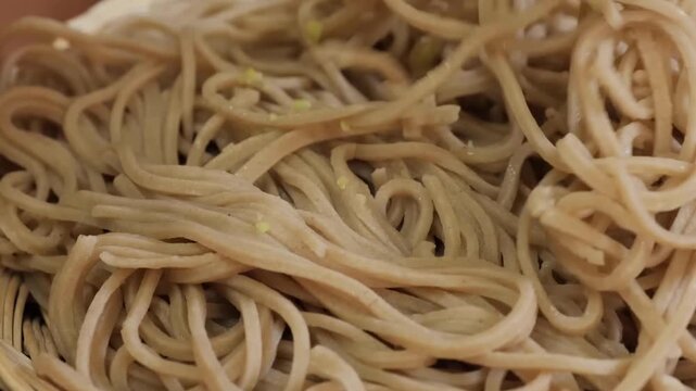 High-angle, close-up footage of authentic Japanese soba noodles made from buckwheat flour. The shot captures the earthy brown texture and thin, long strands of the noodles, representing a staple of tr