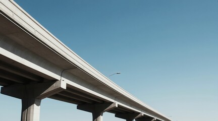 Fototapeta premium Concrete overpass extends into clear blue sky. Elevated highway with strong geometric lines and repetitive pillars creates a modern architectural background for travel and infrastructure themes.