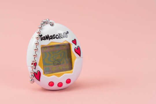Bar, Montenegro: February 6, 2026: White Tamagotchi virtual pet toy with red heart detail on pastel pink background, retro gadget, nostalgia, childhood memory concept.