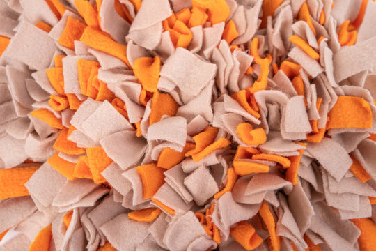 Macro close-up of handmade felt snuffle mat with dense orange and beige fabric strip, pet mental enrichment product texture background concept.