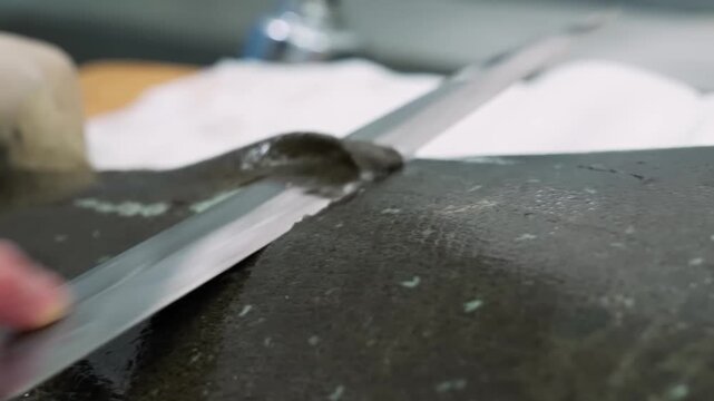A high-quality close-up video capturing the precise culinary technique of a chef using a professional stainless steel fillet knife to skin and debone a fresh whole flatfish on a clean workspace.