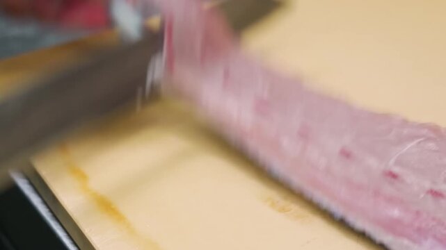 close-up, high-angle shot showing the precise hand movements of a professional chef using a traditional Japanese knife to smoothly remove the skin from a fresh, pink fish fillet on a clean cutting boa