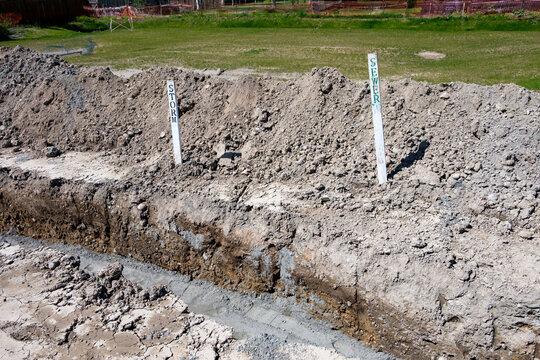 Residential development construction site, trench excavated in ground for underground utilities, sand compacted in the bottom, stakes for storm water and sewer systems installation

