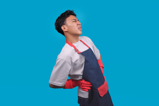 Male Cleaner in an Apron and Rubber Gloves Holding His Lower Back in Pain with Suffering Expression