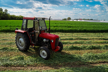 Obraz premium Clean red tractor on growing wheat field with blue sky background, no people