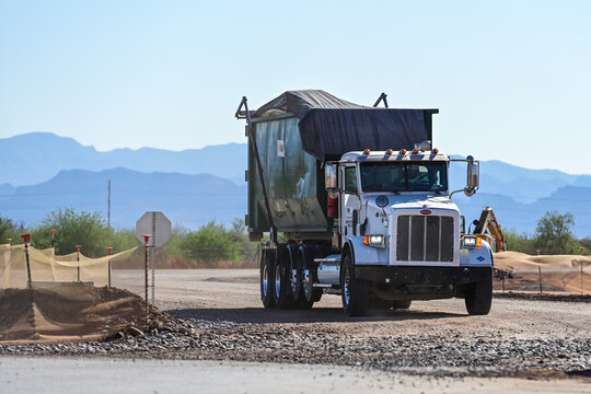 Roll-off truck transporting a large dumpster from a construction site, representing waste removal, debris hauling, and industrial site cleanup operations