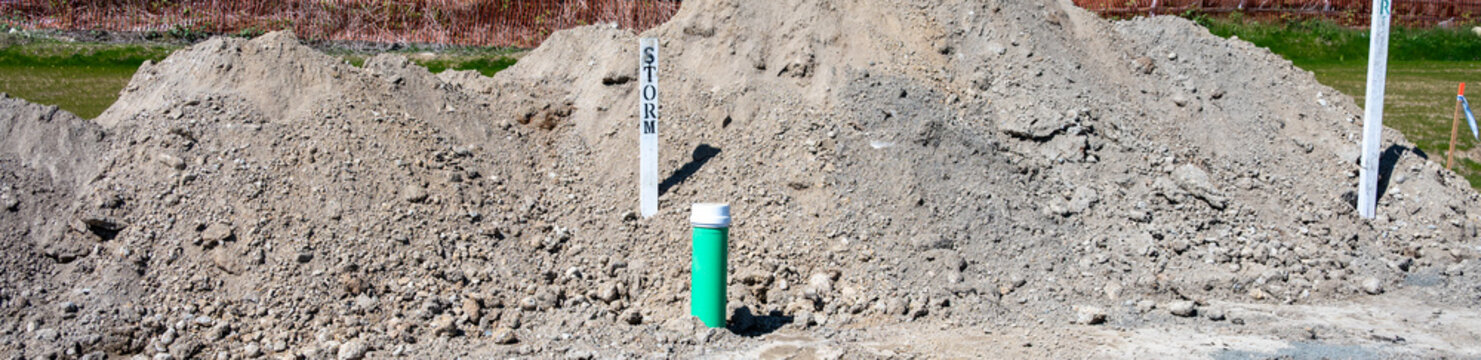 Residential development construction site, trench excavated in ground for underground utilities, 6 inch pipe sticking out for storm drain system
