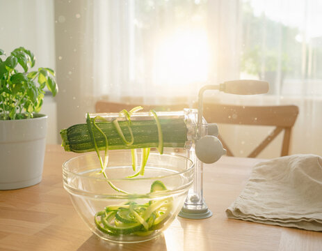 Sustainable plant-based food preparation with zucchini spiralizer on wooden kitchen table with natural light