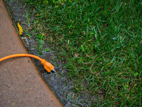 Orange extension cord lying in a puddle on green grass