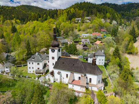 Aerial view of the Church of the Conversion of the Lord and historic houses nestled in lush green hills in Spania Dolina, Banska Bystrica Region, Slovakia.