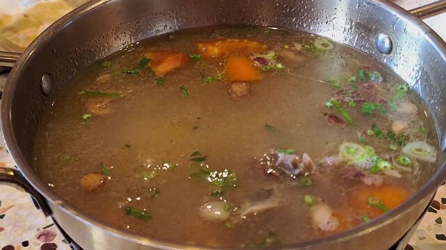 Close-up of hot Sop Iga, an Indonesian beef rib soup, featuring a clear broth with fried shallots, tomatoes, carrots, and celery, served in a bowl.