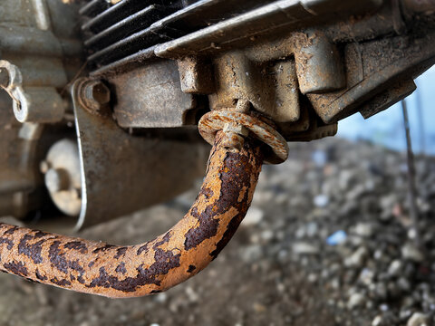 Detailed close-up of an old motorcycle engine showing a cooling fins, and a heavily rusted exhaust pipe.