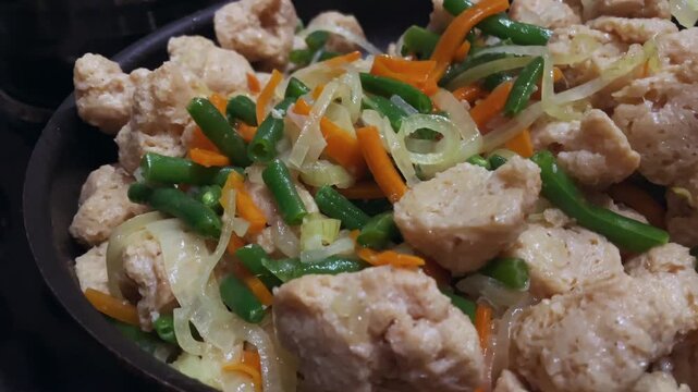 Vegetable stew with soy meat. Green beans, carrots and onions, pan-fried. Vegetarian dish close-up.