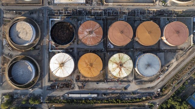 Aerial view of industrial storage tanks with colorful roofs and complex piping at a refinery facility in Cagliari, Sardinia, Italy.