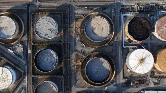 Aerial view of large circular industrial storage tanks and complex piping systems at an oil refinery in Cagliari, Sardinia, Italy.