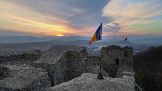 Romanian flag fluttering proudly above a historic citadel at sunset with a beautiful sky motion.