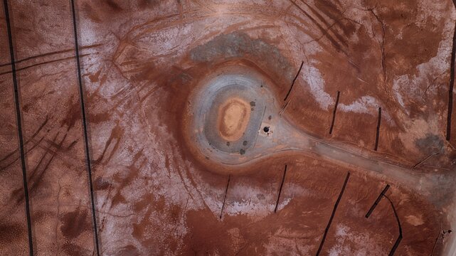 Aerial view of the unique red salt pans with circular structures and tire tracks on the dry earth in Cagliari, Sardinia, Italy.