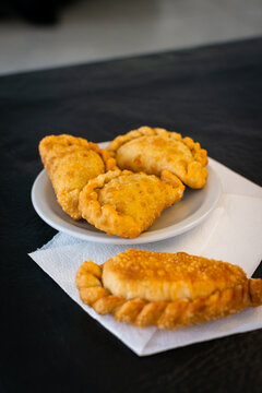Cuatro empanadas fritas doradas servidas en un plato blanco con servilletas de papel sobre una mesa de color negro azabache texturizada.