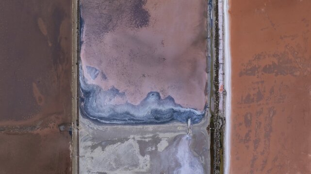 Aerial view of the vibrant pink salt pans and geometric evaporation ponds with salt crusts in Cagliari, Sardinia, Italy.