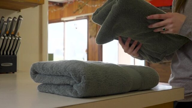A woman gently folds soft towels after cleaning them.