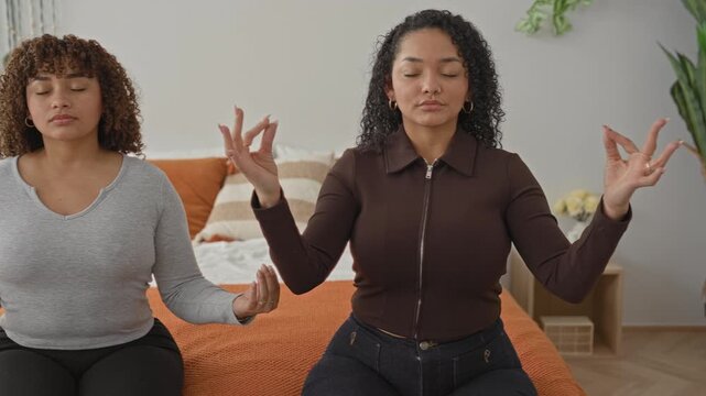 Woman sits crosslegged meditating on bed with hands forming mudra in a building; serenity sisterhood.