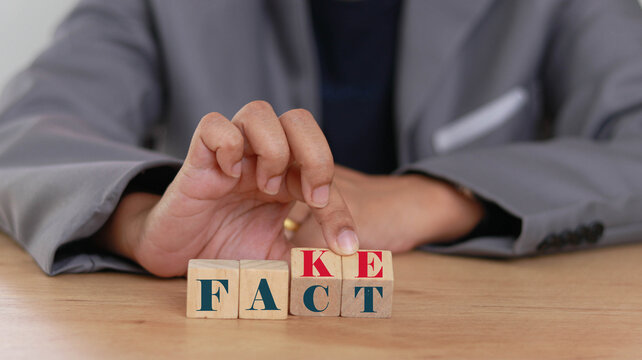 Hand flipping wooden blocks from fact to fake text. Concept of misinformation, fake news, truth distortion, media manipulation, and information credibility in digital society.