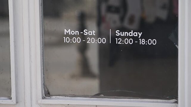 Store hours are shown on the door window in a city