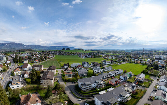 Aerial view of residential houses, green meadows, and distant mountains under a bright sky in Biberist, Solothurn, Switzerland.