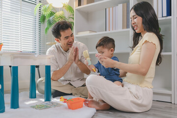 Fototapeta premium Young parents playing with baby using colorful toys at home, encouraging learning and motor skills, showing care, attention, and positive interaction during early childhood development stage.