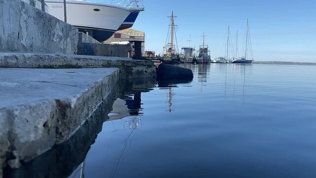 MYKOLAIV, UKRAINE - MAY 22, 2021: Low water-level view of a calm marina with moored boats, a weathered pier, bollard and fender under a clear morning sky
