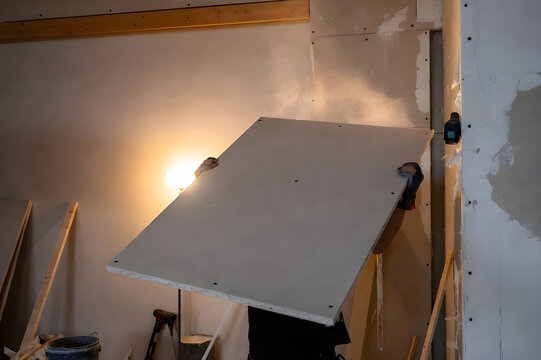 Worker Installing Drywall Sheet With Bright Work Light
