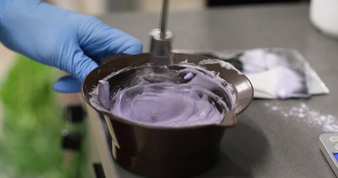 Mixing hair dye. Hairdresser hands. Professional female master in gloves using whisk stirring product in plastic bowl in salon.