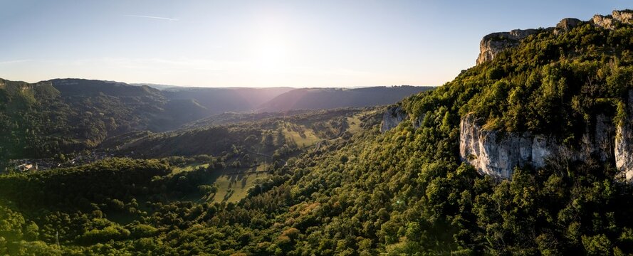 Aerial view of the Loue valley with a historic village nestled between limestone cliffs and dense green forests under a bright sun Lods, Bourgogne-Franche-Com, France.