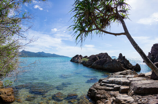 Scenic tropical coast of Koh Chang island with volcanic rock formations, crystal clear turquoise water, and lush greenery under a bright blue sky, Thailand