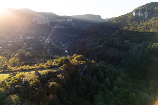 Aerial view of the historic village of Mouthier-Haute-Pierre nestled in a lush valley with rocky cliffs and a winding river during golden hour Lods, Bourgogne-Franche-Comte, France.