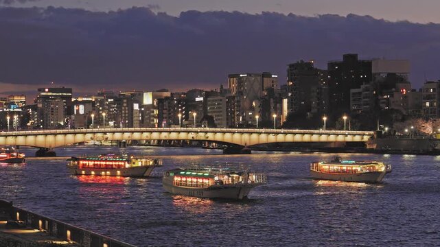 Traditional houseboats with glowing lanterns sail on the Sumida River at night. An illuminated city bridge and Tokyo skyline form a beautiful backdrop.