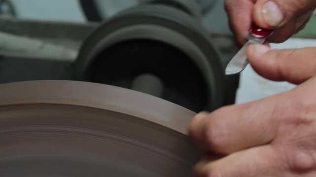 Professional Knife Sharpening in 4K Slow Motion &ndash; Close-Up of Craftsman Honing Folding Knife Blade on Rotating Sharpening Stone, Precision Blade Maintenance Workshop